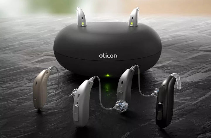 Oticon hearing aids with a charging base behind them